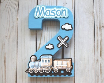 May include: Blue number two with a train and clouds. The number is decorated with the name "Mason".
