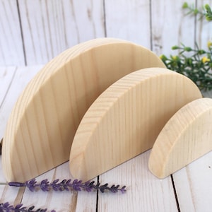 May include: Three unfinished wooden half-circle shapes, stacked in descending size, with the largest at the back and the smallest in front. The wood has a natural, light brown color.