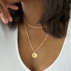 Może przedstawiać: Złoty naszyjnik z łańcuszkiem i okrągłym wisiorem z literą L.