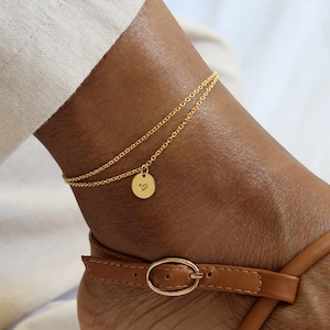 Puede incluir: Tobillera de oro con una cadena delicada y un pequeño dije en forma de corazón.