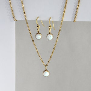 May include: A gold chain necklace and matching earrings with a white opal pendant and earrings.