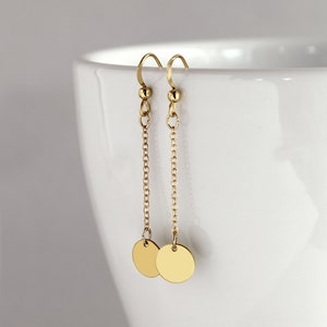 Peut inclure: Boucles d'oreilles pendantes dorées avec un petit disque rond à l'extrémité de chaque chaîne.