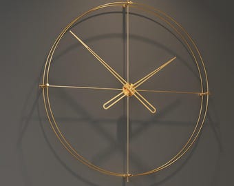 May include: A large, gold-colored, minimalist wall clock with a circular design. The clock features thin, elegant hands and a simple, modern aesthetic. It is mounted on a gray wall, with a cityscape visible through a window in the background.