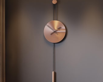 May include: A modern wall clock with a copper-colored face and a pendulum hangs above a black, curved bench. The clock's hands are black. A small, light-colored sculpture rests on the bench. The wall is a dark gray color.