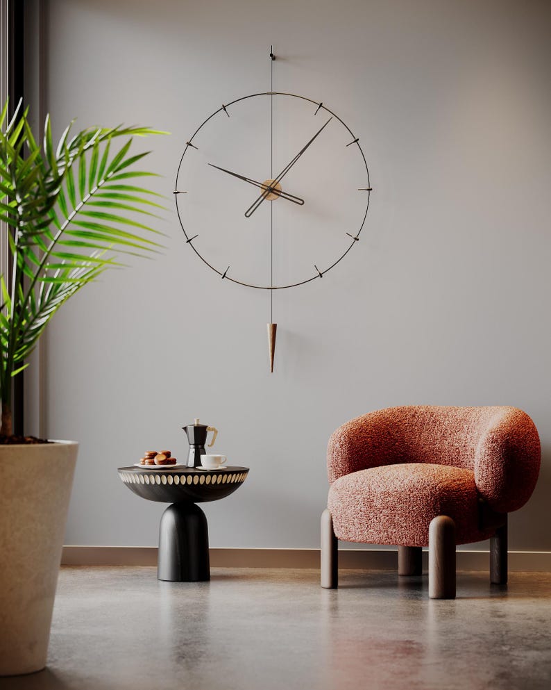 May include: A contemporary wall clock with a black metal frame and hands, hanging on a wall. The clock features a pendulum and is positioned above a small table with a coffee pot and pastries. A peach armchair is also visible.