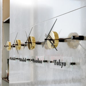 May include: A wall mounted clock with four gold clock faces and black hands. The clock faces are labelled with the cities New York, Istanbul, London, and Tokyo.