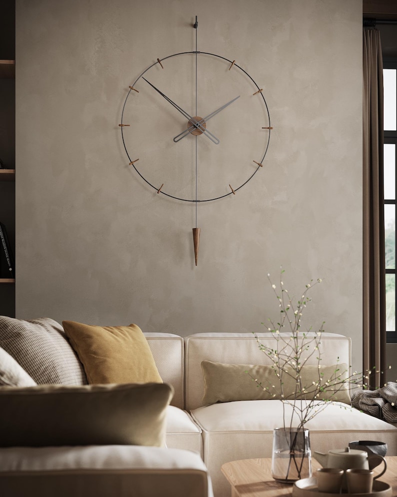 May include: A contemporary wall clock with a black metal frame and a wooden centre. The clock features a pendulum and is suspended on a neutral wall. The clock is above a cream sofa with yellow and green cushions. The clock's diameter is approximately 60 cm.