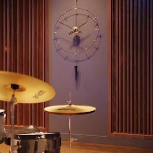May include: A contemporary wall clock with a minimalist design. It has a gold-coloured centre and hands, with black lines indicating the hours. A dark blue, cone-shaped pendulum hangs below. The background includes wooden panelling and a drum kit.
