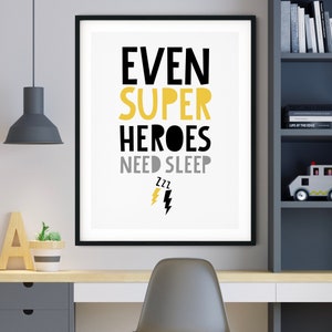 May include: A framed print with the words "EVEN SUPER HEROES NEED SLEEP" in black, yellow, and gray. The print includes a lightning bolt and ZZZ symbols. The artwork is displayed on a desk in a child's room.
