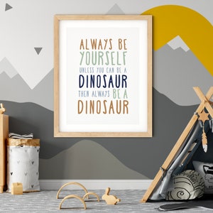 May include: A framed print with a light blue background and brown wood frame. The print features a motivational quote in a playful font: "Always be yourself unless you can be a dinosaur, then always be a dinosaur."