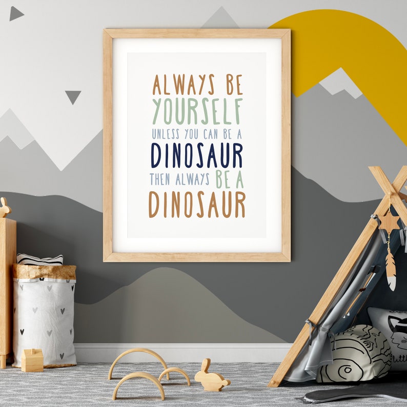 May include: A framed print with a light blue background and brown wood frame. The print features a motivational quote in a playful font: "Always be yourself unless you can be a dinosaur, then always be a dinosaur."