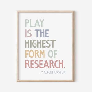 May include: A framed print featuring the quote "PLAY IS THE HIGHEST FORM OF RESEARCH." in various pastel colours. The quote is attributed to Albert Einstein. The print is in a light wood frame with a white background.
