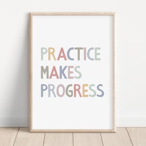 Op de afbeelding: Een ingelijste print met de tekst "PRACTICE MAKES PROGRESS" in kleurrijke blokletters. De tekst is in pastelkleuren: geel, roze, groen, blauw en perzik. De lijst is licht van kleur.