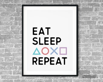 May include: Black framed print with white background and the text "Eat Sleep Repeat" in black. The text is surrounded by four colorful symbols: a blue triangle, a red circle, a black X, and a purple square.