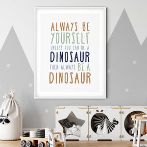 May include: A framed print with the text "Always be yourself unless you can be a dinosaur then always be a dinosaur" in blue, green, and brown text on a white background.