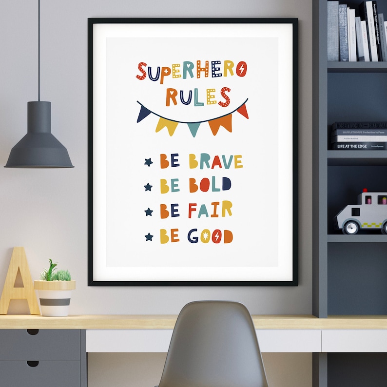 Op de afbeelding: Een kleurrijke printable poster met de tekst "SUPERHERO RULES" en een string vlaggen boven de tekst. Onder de tekst staan vier regels: "BE BRAVE", "BE BOLD", "BE FAIR" en "BE GOOD".