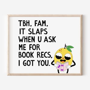 May include: A framed print featuring a cartoon lemon character holding a book. The print has the text "TBH, FAM, IT SLAPS WHEN U ASK ME FOR BOOK RECS, I GOT YOU" in black font on a white background.