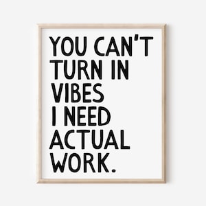 May include: A framed print with the text "YOU CAN'T TURN IN VIBES I NEED ACTUAL WORK" in bold black letters on a white background. The frame is a light wood color.