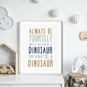 May include: White framed print with the text "Always be yourself unless you can be a dinosaur then always be a dinosaur" in various colors on a white background.