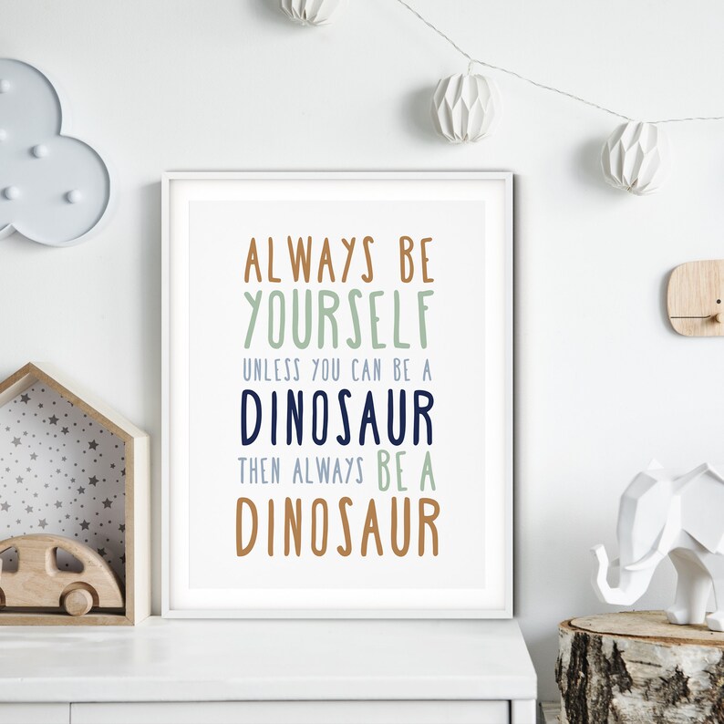 May include: White framed print with the text "Always be yourself unless you can be a dinosaur then always be a dinosaur" in various colors on a white background.