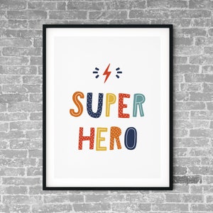 以下が含まれることがあります： 白い背景にカラフルな文字で「SUPER HERO」と書かれた額装されたプリント。文字の上に稲妻が描かれている。