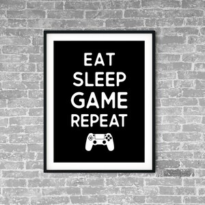 Könnte beinhalten: Schwarz-weiß gerahmter Druck mit dem Text "Eat Sleep Game Repeat" und einem weißen Videospiel-Controller-Symbol.