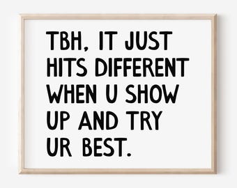 May include: A framed print with the text "TBH, IT JUST HITS DIFFERENT WHEN U SHOW UP AND TRY UR BEST." The text is in black, bold font on a white background, and framed in a light wood frame.