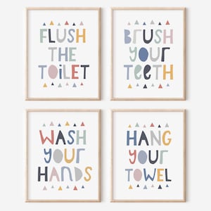 Może przedstawiać: Cztery oprawione wydruki z kolorowym tekstem i geometrycznymi kształtami. Wydruki głosi: "Flush the Toilet", "Brush Your Teeth", "Wash Your Hands" i "Hang Your Towel".