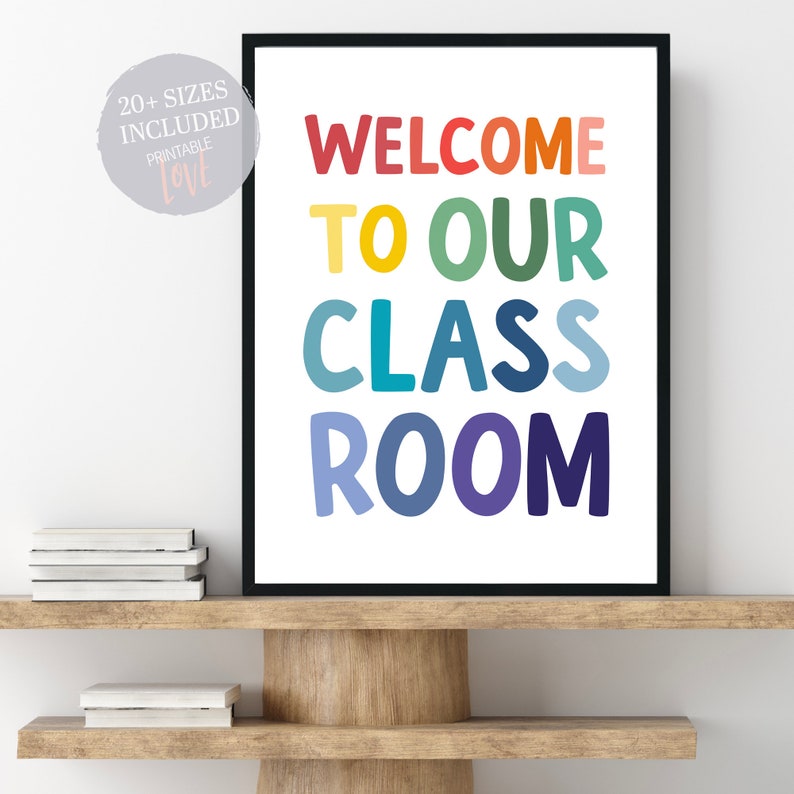 May include: A colorful classroom sign with the text "Welcome to our classroom" in rainbow colors. The sign is framed in black and is sitting on a wooden shelf.