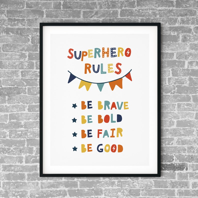Op de afbeelding: Een witte printable poster met de tekst "SUPERHERO RULES" in kleurrijke letters. De poster heeft een reeks kleurrijke vlaggen en een lijst met regels: "BE BRAVE", "BE BOLD", "BE FAIR" en "BE GOOD".