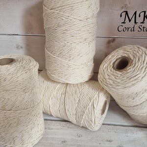 May include: Four spools of natural coloured twine with gold flecks. The twine is wound tightly on the spools. The spools are on a wooden surface.