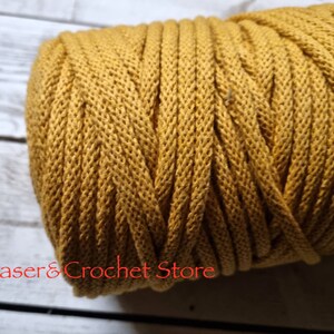 May include: A close-up of a spool of mustard yellow cotton cord. The cord is tightly wound and has a textured surface.