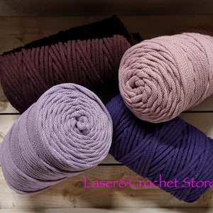 May include: Four spools of cotton rope in different colours: dark brown, light purple, dusty rose, and navy blue. The spools are arranged in a wooden box.