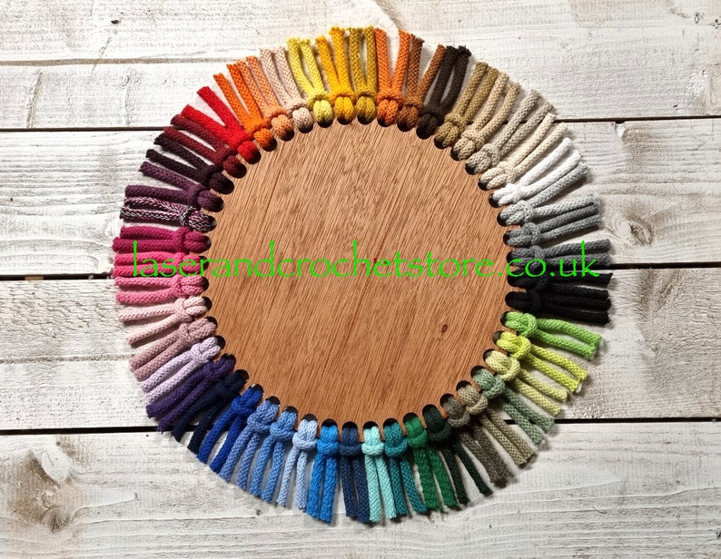 May include: A wooden circle with a variety of colours of cotton cord tied in knots around the edge. The cord is arranged in a rainbow pattern. The text "laserandcrochetstore.co.uk" is printed on the circle.