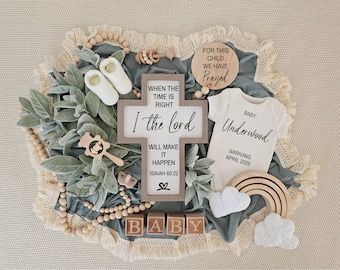 May include: A baby announcement featuring a wooden cross with the inscription "When the time is right, I the Lord will make it happen, Isaiah 60:22". A white babygrow reads "Baby Underwood, Arriving April 2025". The announcement is surrounded by wooden beads, a wooden rainbow, and a green plant.