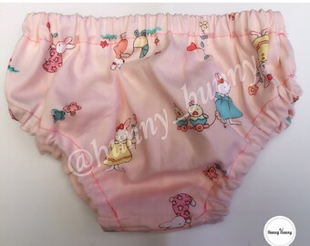Puede incluir: Braguitas de bebé de color rosa con una cintura elástica blanca y un estampado de conejos y otros animales. Las braguitas tienen un ribete rosa alrededor de los bordes.