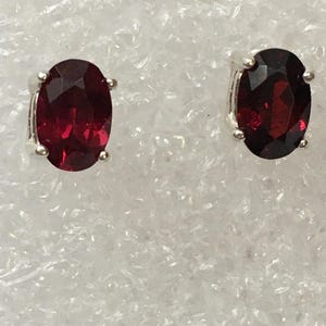 May include: A pair of silver stud earrings with oval-shaped red gemstones.