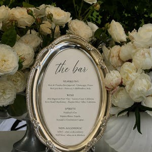 May include: An oval silver-toned metal tray with a decorative beaded edge, displaying a printed menu titled the bar. The menu lists sparkling, wine, spirits, and non-alcoholic beverage options including Moët & Chandon, Pinot Noir, and Hendrick's Gin.