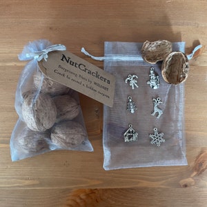 May include: A set of Christmas nutcrackers in a white organza bag. The bag contains six walnuts and a tag that reads "Nut Crackers Surprising Nuts by WALMART Crack to reveal a hidden surprise". The bag is next to a white organza bag with six silver Christmas charms.