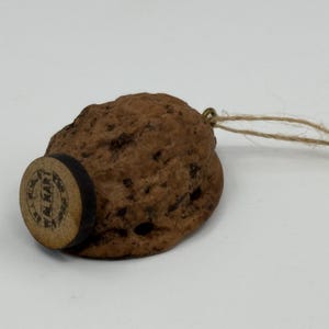 May include: A handcrafted bottle stopper made from a walnut shell, featuring a wooden base with the text "W. MART" in a circular design. A thin twine loop is attached for easy removal.
