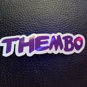 May include: A purple sticker with the word "THEMBO" written in a bold, stylized font.