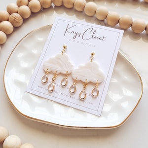 May include: White cloud shaped earrings with gold accents and clear crystal raindrop charms. The earrings are handmade and the text "Kayz Closet Creates" is on the card.