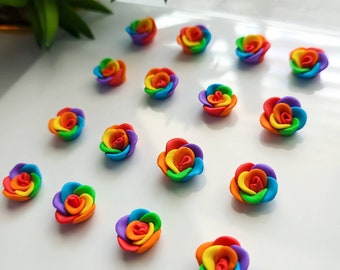 May include: A collection of 15 rainbow-colored clay roses. Each rose is made of six layers of clay in the colors of the rainbow, with the red layer on the outside and the violet layer on the inside. The roses are arranged in a random pattern on a white surface.