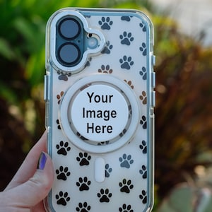 May include: A clear phone case featuring a repeating pattern of black paw prints. The case includes a circular white magnetic charging ring in the center with the black text Your Image Here printed on it and a camera cutout at the top.