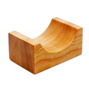 Może przedstawiać: Drewniany stojak z zakrzywionym, wydrążonym środkiem, zaprojektowany do trzymania małego przedmiotu. Stojak wykonany jest z jasnobrązowego drewna z naturalnym usłojeniem.