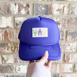 May include: Purple trucker hat with a white patch featuring three embroidered lobsters in green, purple and yellow.