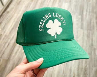 May include: Green trucker hat with a white four-leaf clover and the text "Feeling Lucky!"
