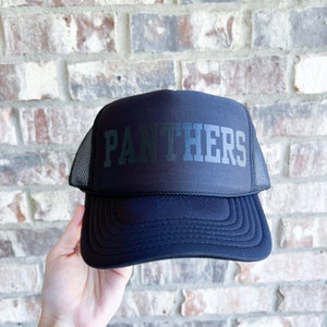 Può includere: Cappellino da camionista nero con rete nera sul retro e la scritta "PANTHERS" in lettere bianche.
