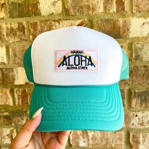 Puede incluir: Gorra de camionero blanca y turquesa con un parche rosa, arcoíris y blanco que dice "Hawaii Aloha Aloha State".