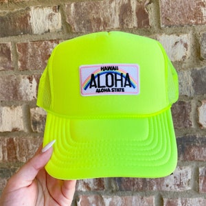 Puede incluir: Gorra de camionero de color amarillo neón con un parche de arcoíris que dice "Hawaii Aloha State" en texto negro.